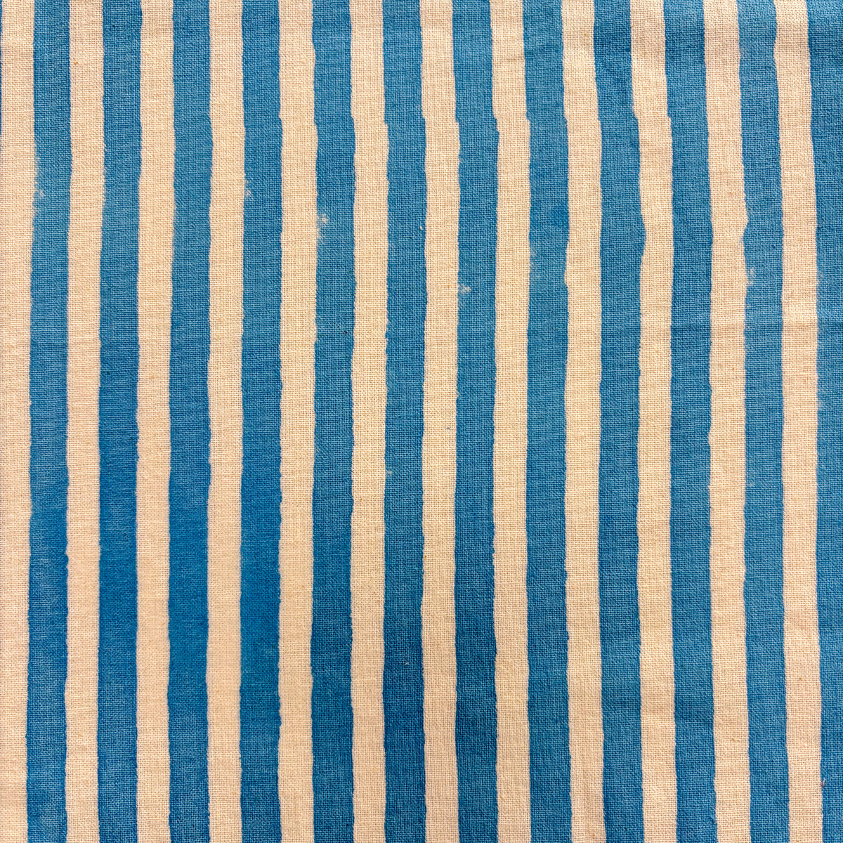 A close-up of a striped textile pattern featuring alternating vertical stripes in medium blue and warm beige with a visible woven texture.