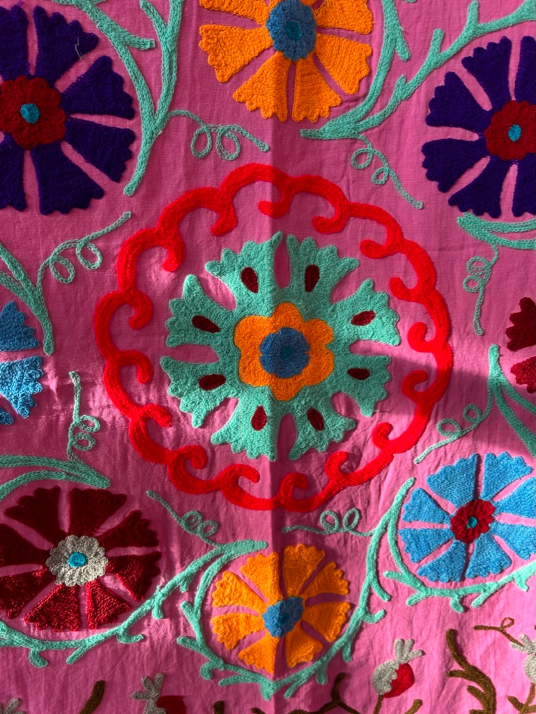 Close-up of a colorful embroidered fabric with floral patterns on a pink background