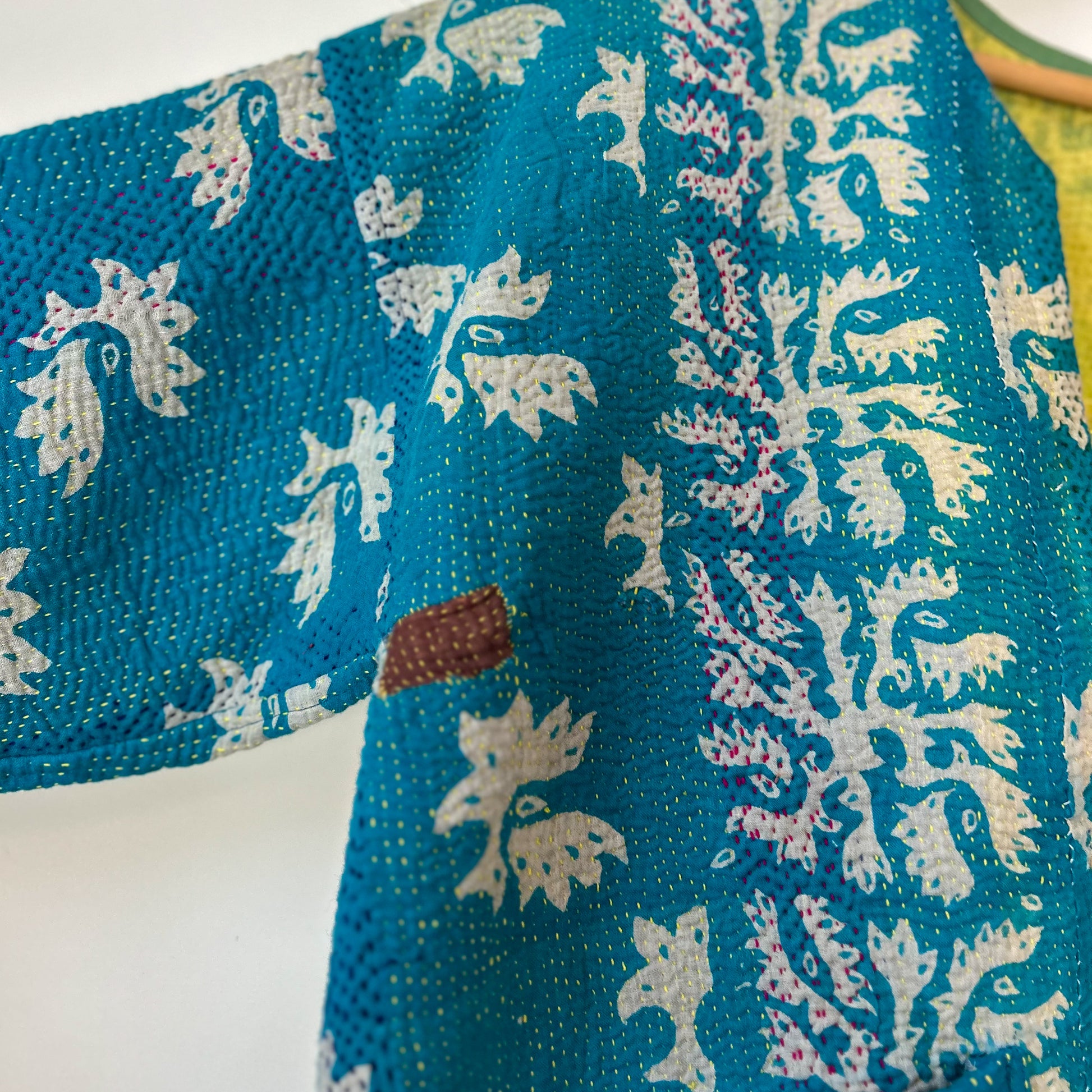 Blue fabric with white floral patterns on a white background. Vintage-kantha-jacket-handmade-unique-38-turquoise-pattern-stitching