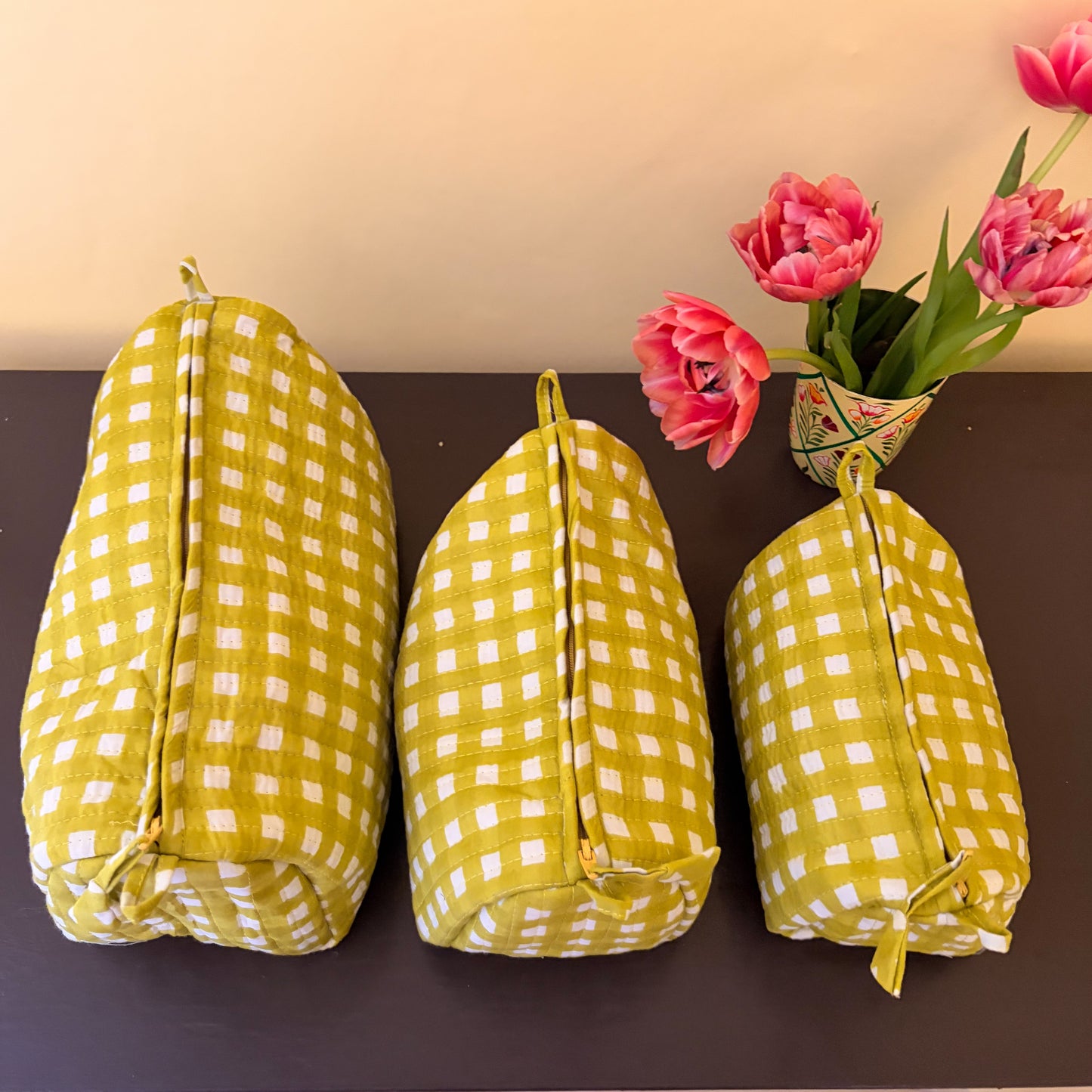 Three yellow and white checkered bags on a dark surface with pink tulips in the background.