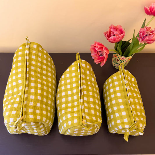 Three yellow and white checkered bags on a dark surface with pink tulips in the background.