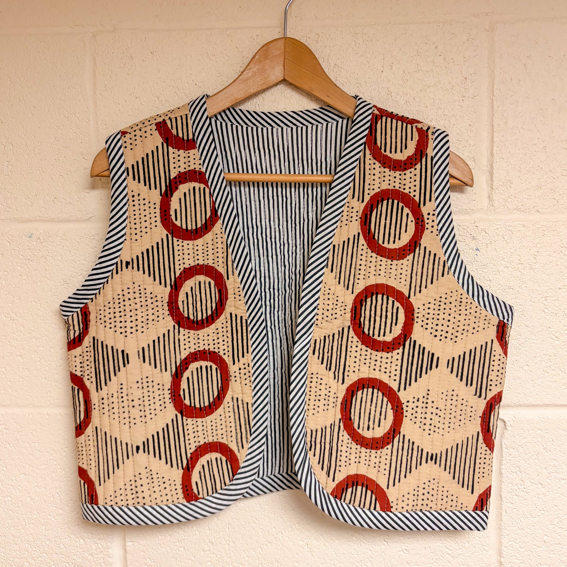  patterned vests hanging on a wooden hanger against a beige wall.