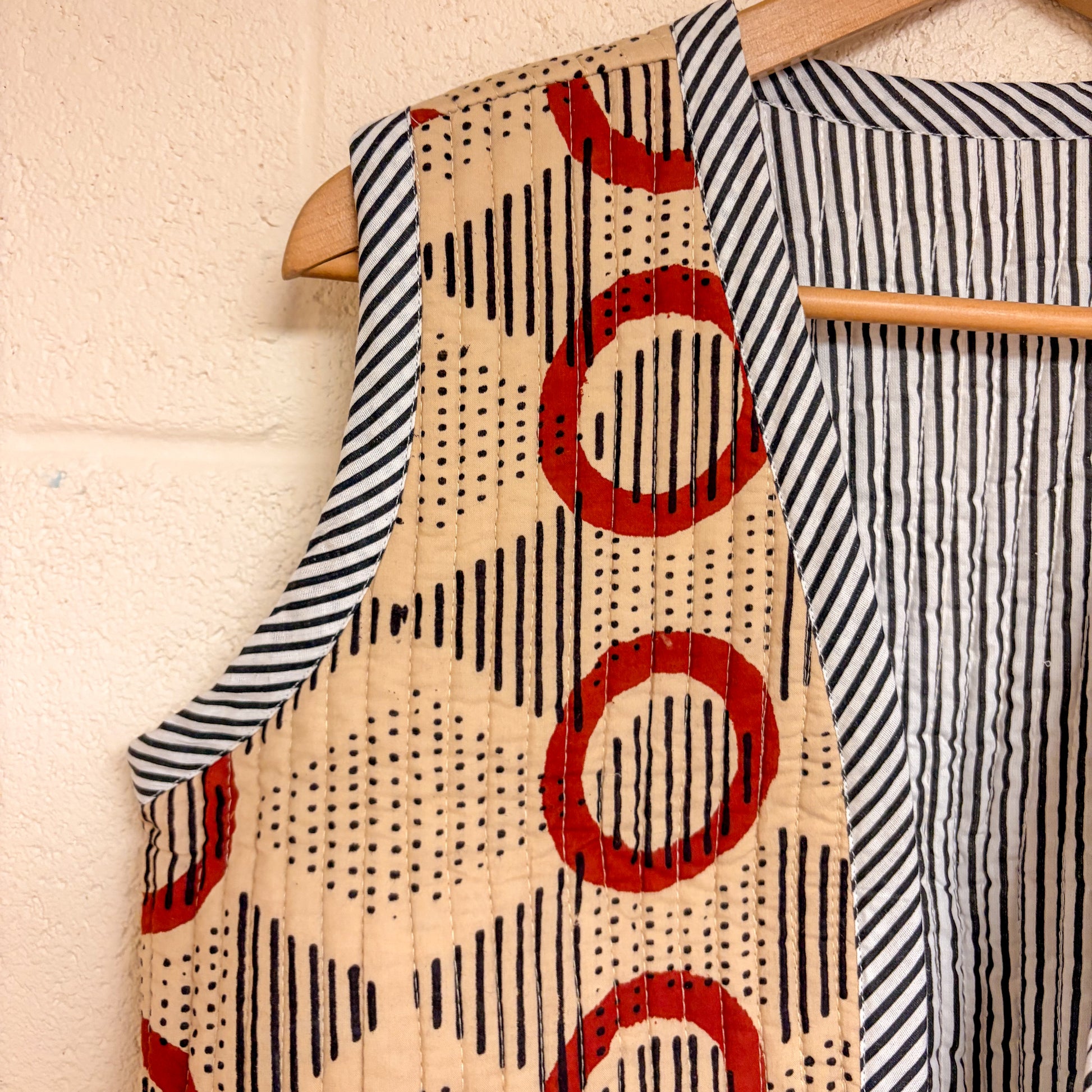 waistcoat hanging on a wooden hanger against a light background.