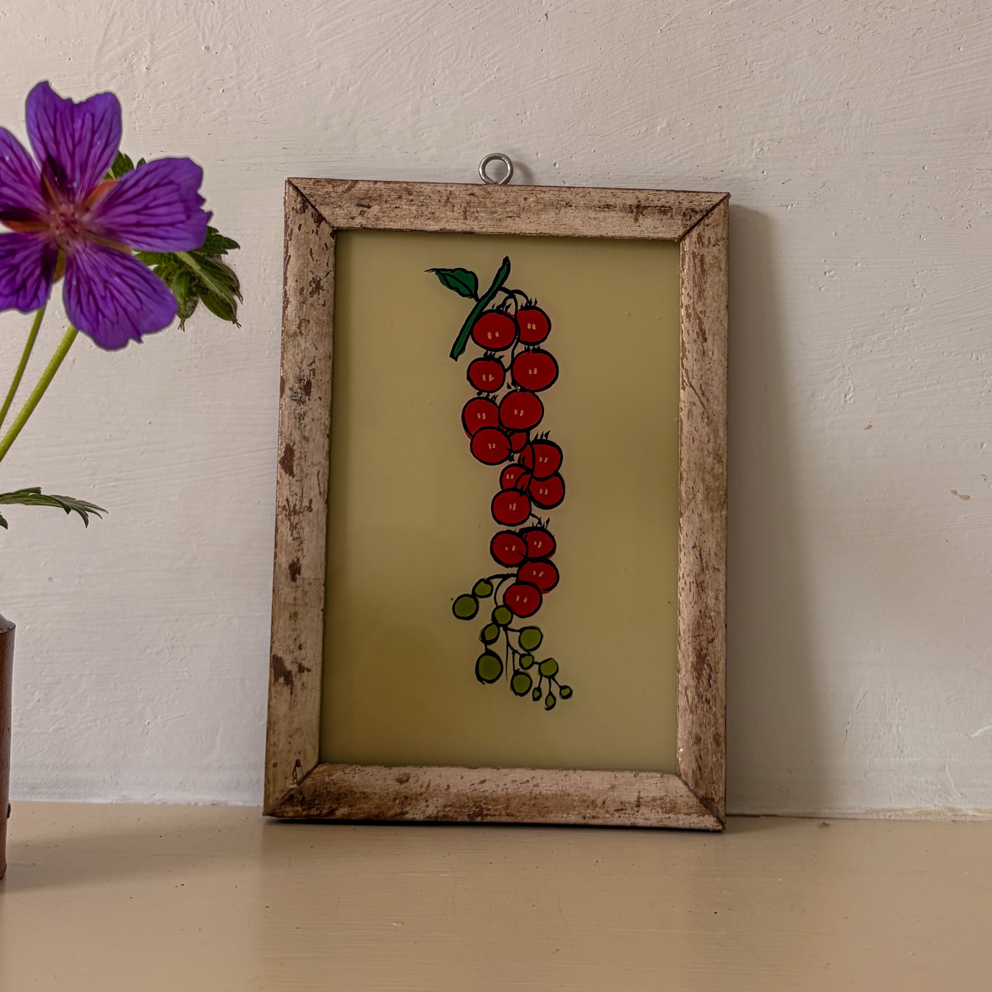 Framed artwork of red berries on a beige background with a purple flower to the left.