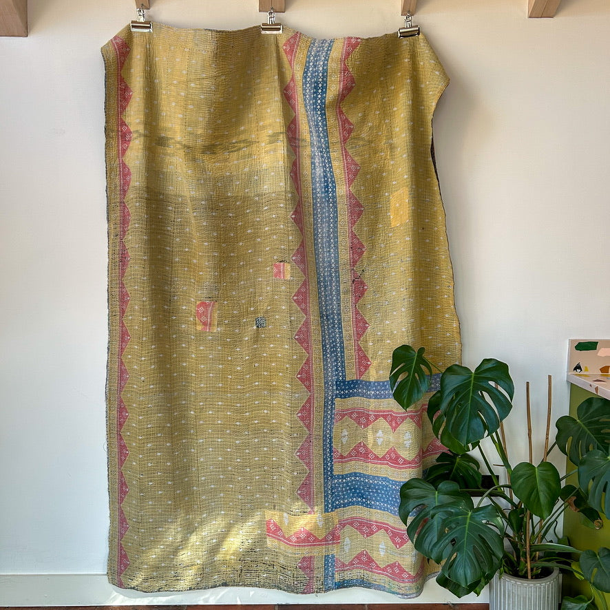 Colorful patterned fabric on a mannequin with a plant in the background. kantha-vintage-2031 - hand-made-blanket-throw-textiles-wall-hanging